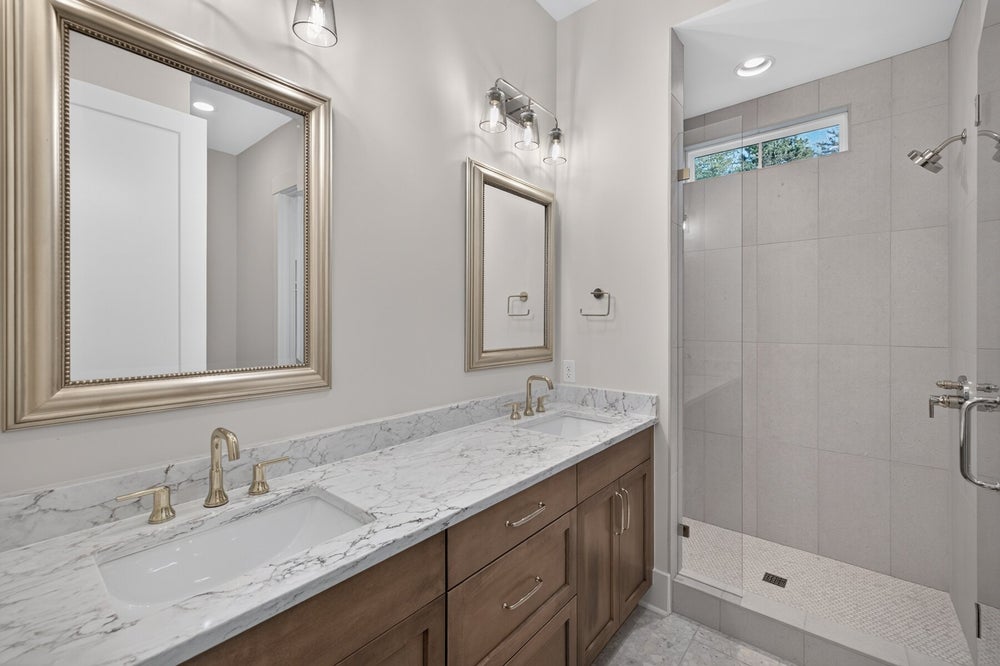 Bathroom with double sink vanity, marble countertop, wood cabinets, and walk-in tile shower with glass enclosure