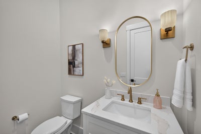 Powder room with white marble vanity, gold fixtures, oval mirror, and wall sconces