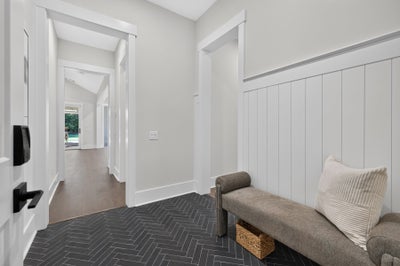 Mudroom entryway with dark herringbone tile floor, shiplap wainscoting, and upholstered bench with storage basket