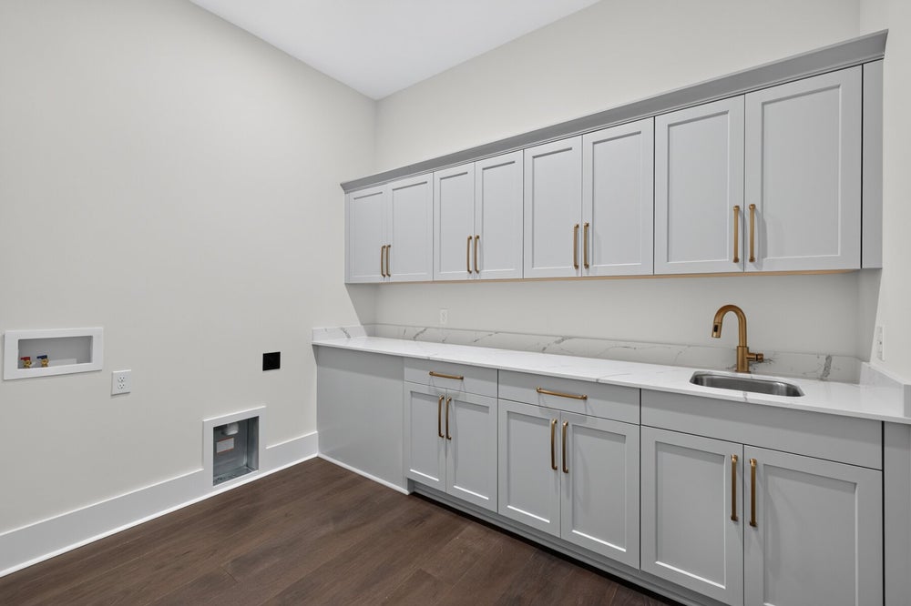 Laundry room with gray cabinets, marble countertop, gold hardware, and utility sink on dark hardwood floors