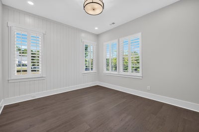 Empty room with dark hardwood floors, white plantation shutters, and shiplap accent wall