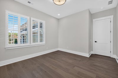 Empty bedroom with dark hardwood floors, gray walls, and white plantation shutters on corner windows.