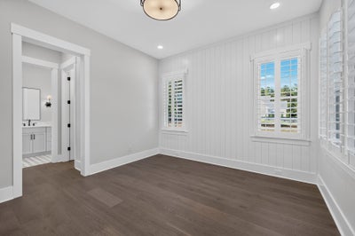 Empty bedroom with dark hardwood floors, shiplap accent wall, plantation shutters, and ensuite bathroom access.