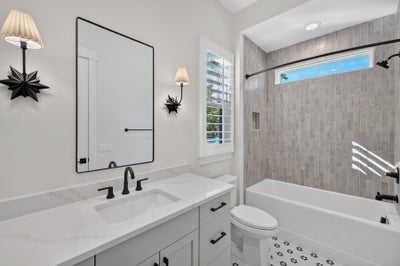 Bathroom with white vanity, quartz countertop, tub-shower combo with gray tile, and black fixtures
