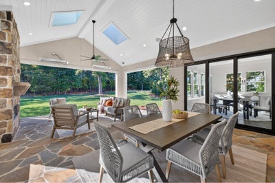 Covered outdoor patio with dining table, stone fireplace, vaulted ceiling with skylights, and open views to backyard.