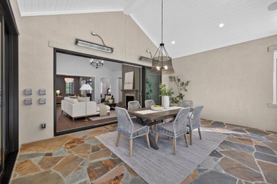 Covered outdoor dining area with stone floor, six-chair table, and open sliding doors to living room inside.