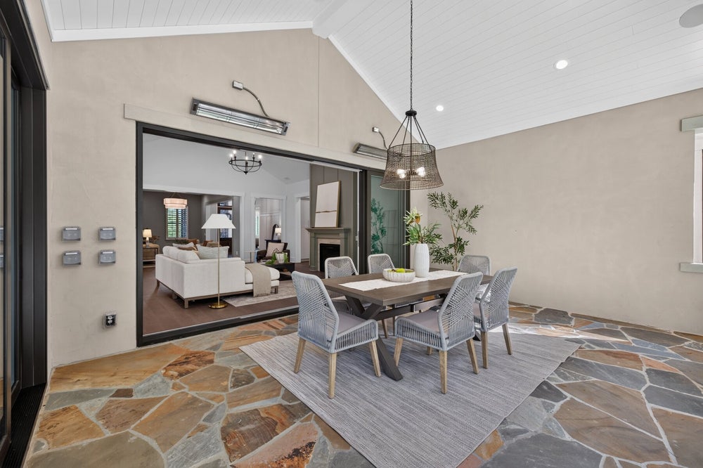 Covered outdoor dining area with stone floor, six-chair table, and open sliding doors to living room inside.
