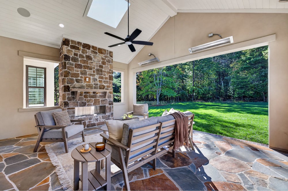 Covered patio with stone fireplace, ceiling fan, seating area, and open view of backyard lawn