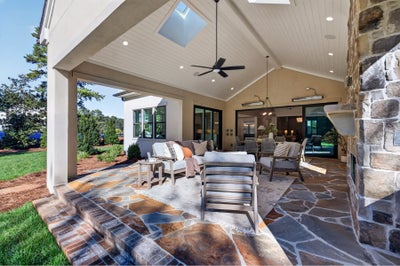 Covered outdoor patio with stone fireplace, vaulted ceiling, ceiling fan, and seating area on flagstone floor