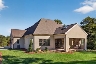 Single-story home with beige stucco exterior, dark hip roof, and covered patio with stone accent wall and green lawn