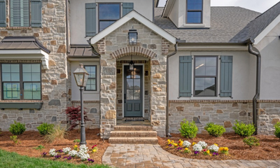 Stone and stucco home exterior with arched front entry, blue shutters, and landscaped flower beds.