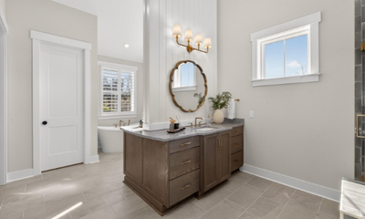 Spacious master bathroom with double vanity, round mirror, gold light fixture, and freestanding soaking tub in background.