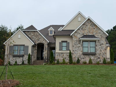 Single-story home with stone and stucco exterior, arched entry, gray shutters, and manicured front lawn