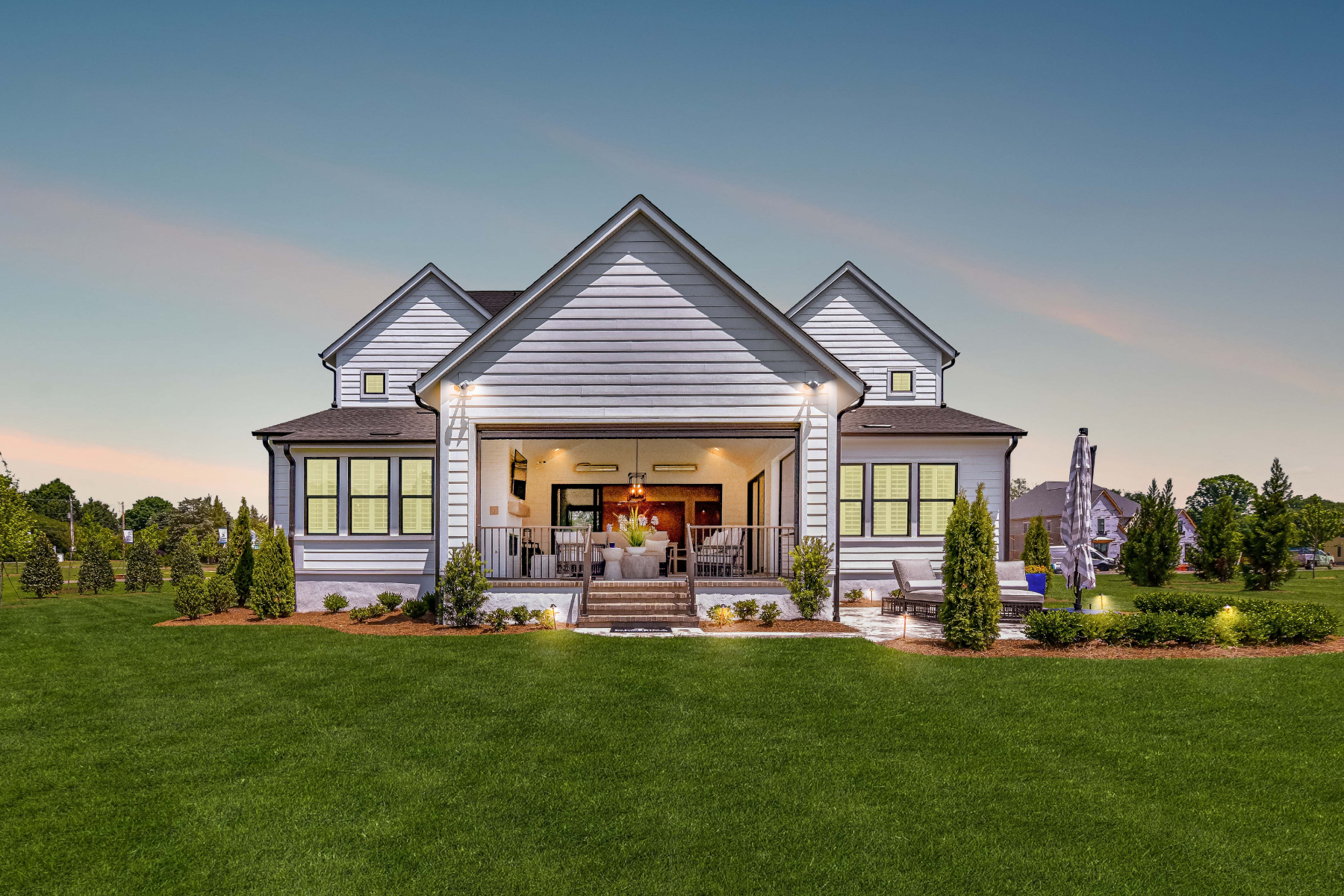 White craftsman-style home with three gabled roofs and covered outdoor living area at dusk