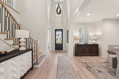 Two-story foyer with light wood floors, black front door, and modern pendant light