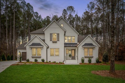 Two-story white brick home with gray shutters and metal roof accents on wooded lot