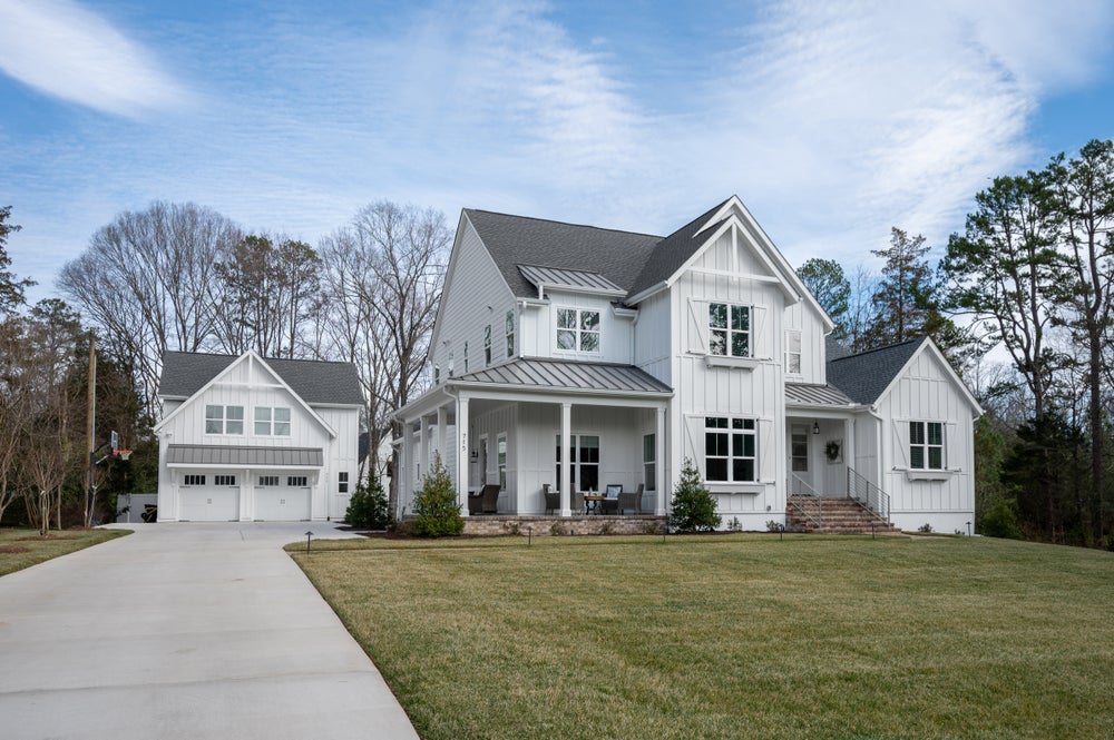 Two-story white farmhouse with board and batten siding, covered front porch, and detached two-car garage