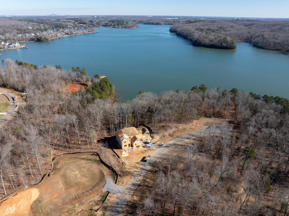 Aerial view of home under construction on wooded lakefront lot