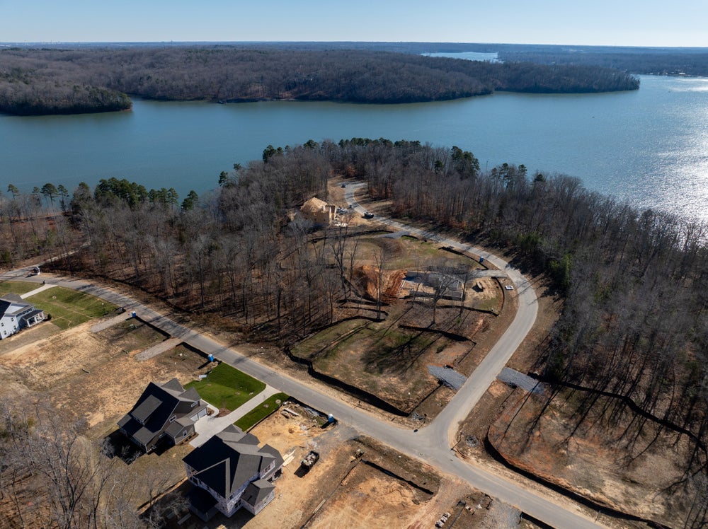 Aerial view of lakefront residential development with homes under construction on wooded peninsula