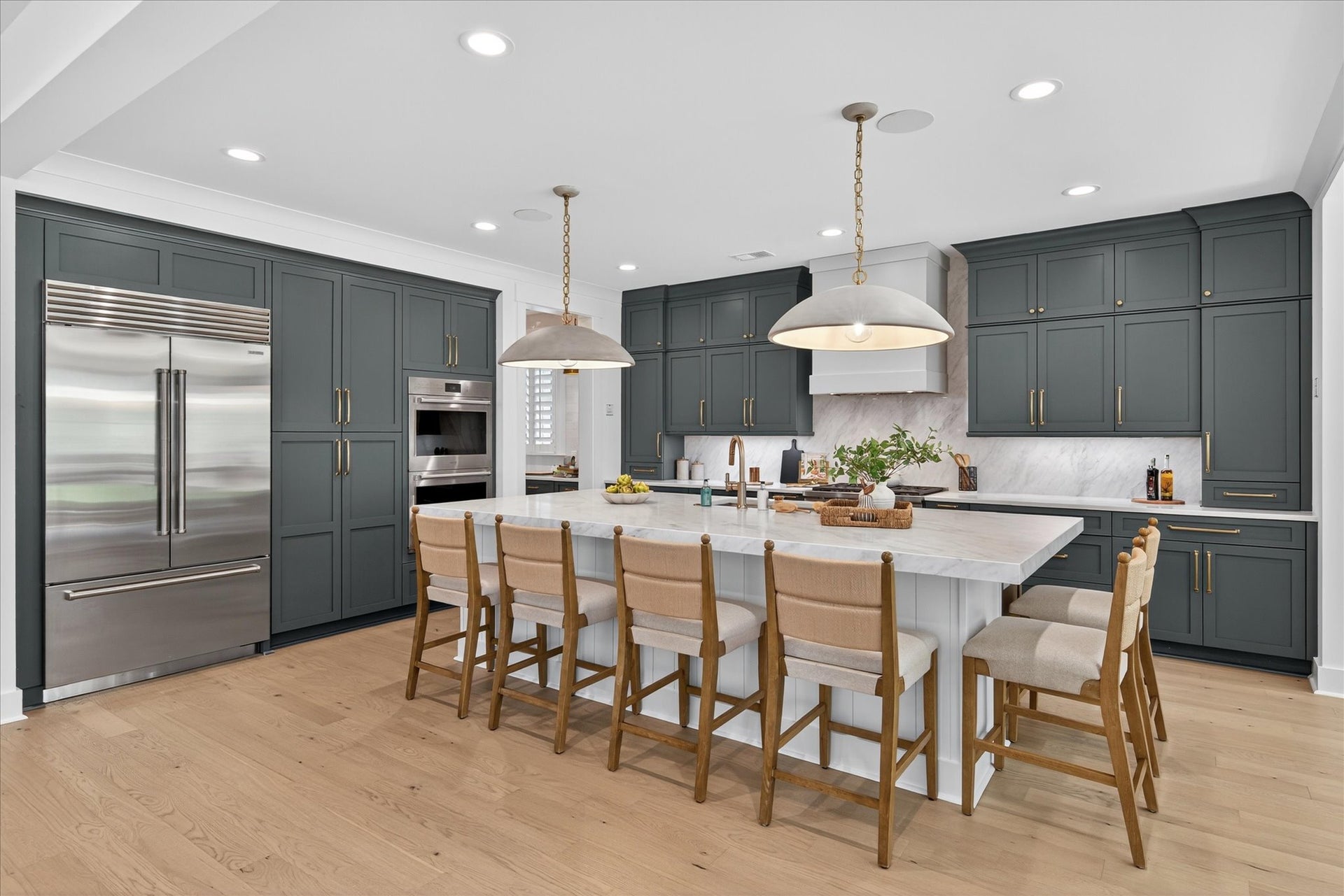 Kitchen with gray cabinets, white marble island, stainless appliances, and wood bar stools