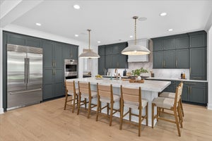 Kitchen with gray cabinets, white marble island, stainless appliances, and wood bar stools