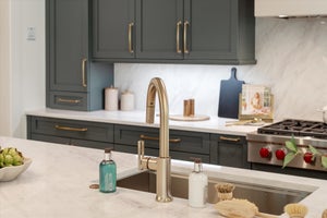 Modern kitchen with gray cabinets, white countertops, gold hardware, and stainless steel appliances