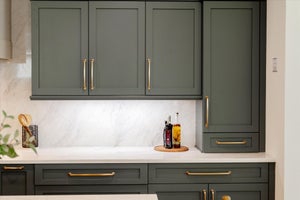 Sage green kitchen cabinets with brass hardware and white marble countertops