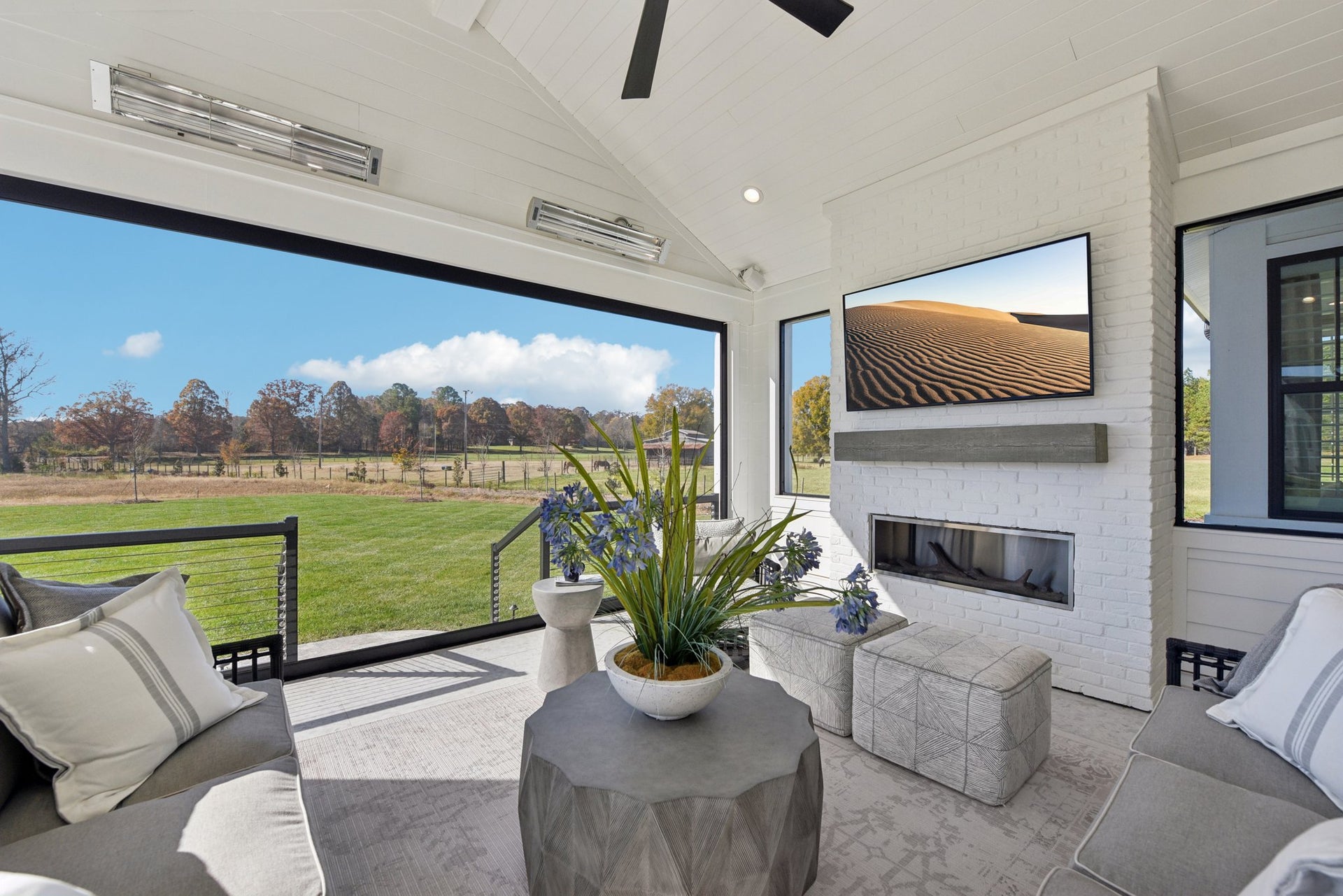 Covered outdoor patio with fireplace, ceiling fan, and large windows overlooking grassy yard