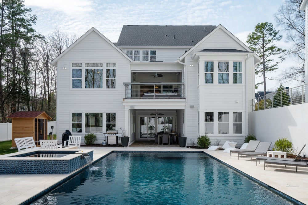 Two-story white home with covered balcony overlooking backyard pool and patio area