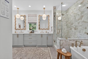 Master bathroom with gray double vanity, gold mirrors, marble shower, and soaking tub