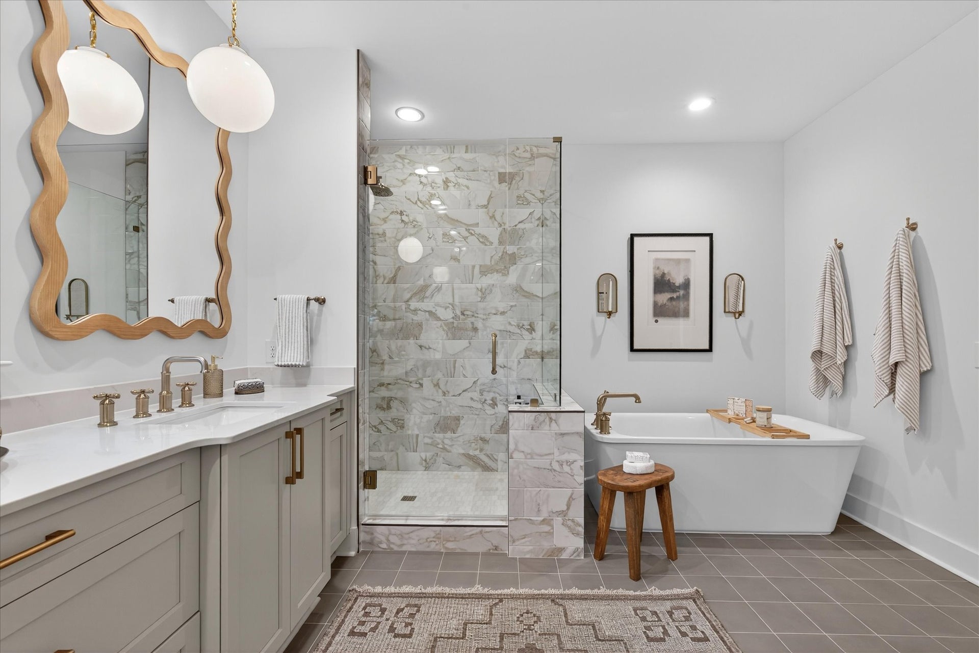 Modern bathroom with marble shower, freestanding tub, gray vanity, and brass fixtures