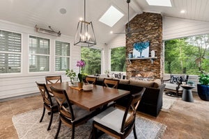 Covered patio with dining table, stone fireplace, vaulted ceiling, and skylights