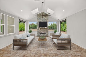 Covered patio with vaulted ceiling, stone fireplace, brick pavers, and modern outdoor furniture