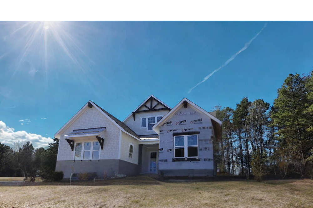 Single-story home under construction with white siding and Tudor-style gable detail