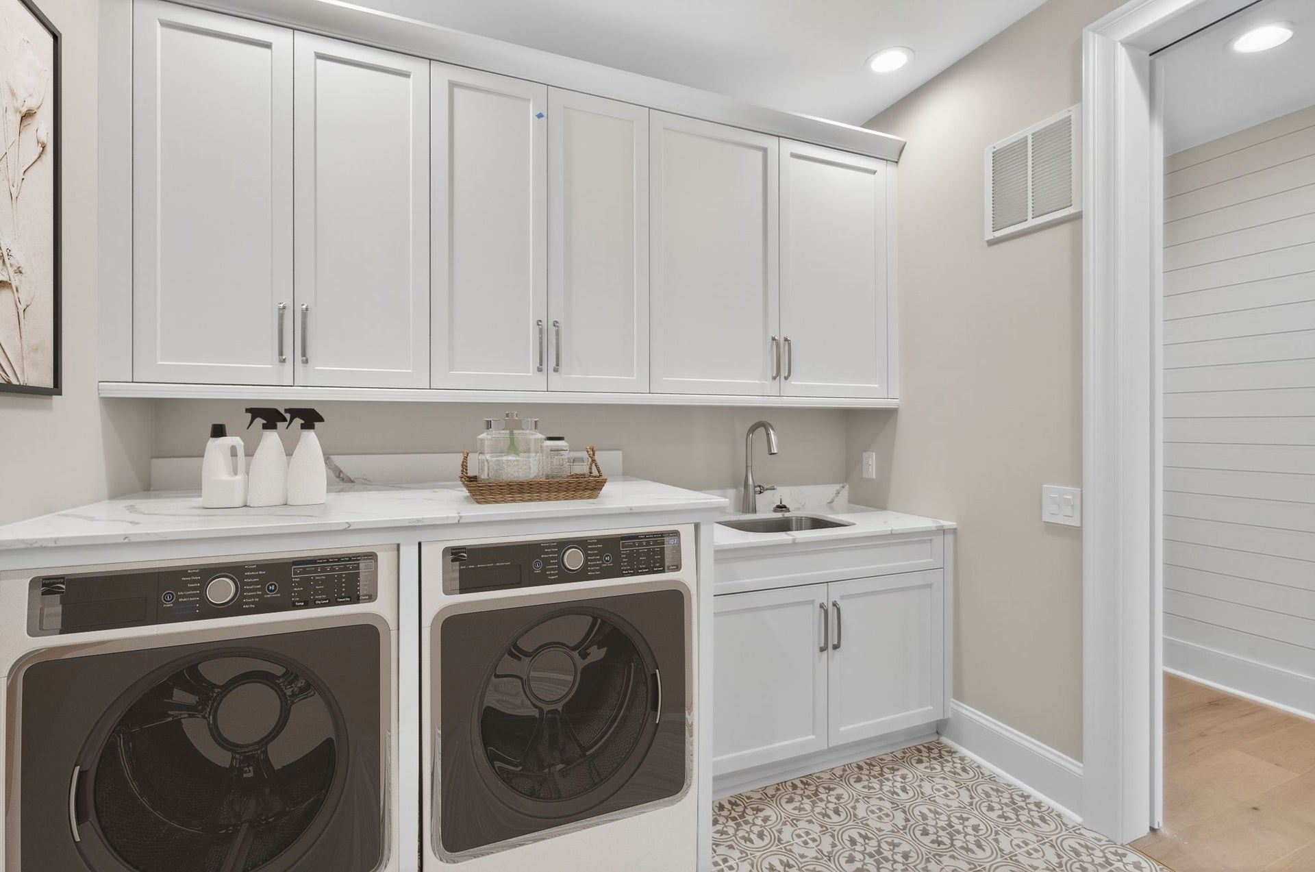 Laundry room with white cabinets, stainless steel appliances, and undermount sink with patterned tile floor