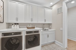 Laundry room with white cabinets, stainless steel appliances, and undermount sink with patterned tile floor
