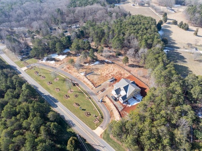 Aerial view of new home under construction on wooded lot with cleared land and equipment