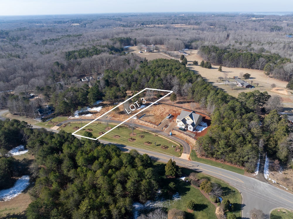 Aerial view of wooded building lot outlined in white with nearby home under construction