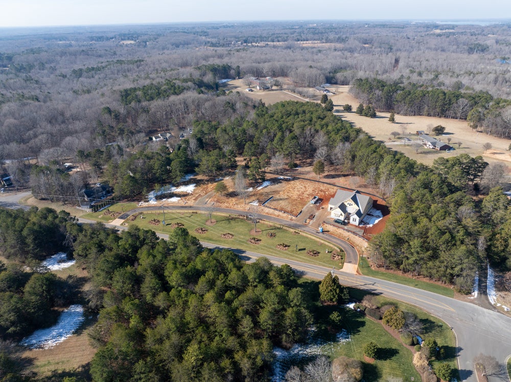 Aerial view of new home under construction on wooded lot with cleared driveway