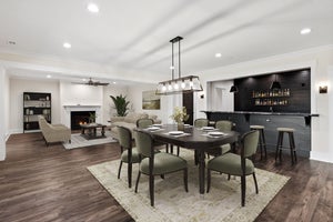 Open-concept living and dining area with dark wood floors, tray ceiling, and wet bar