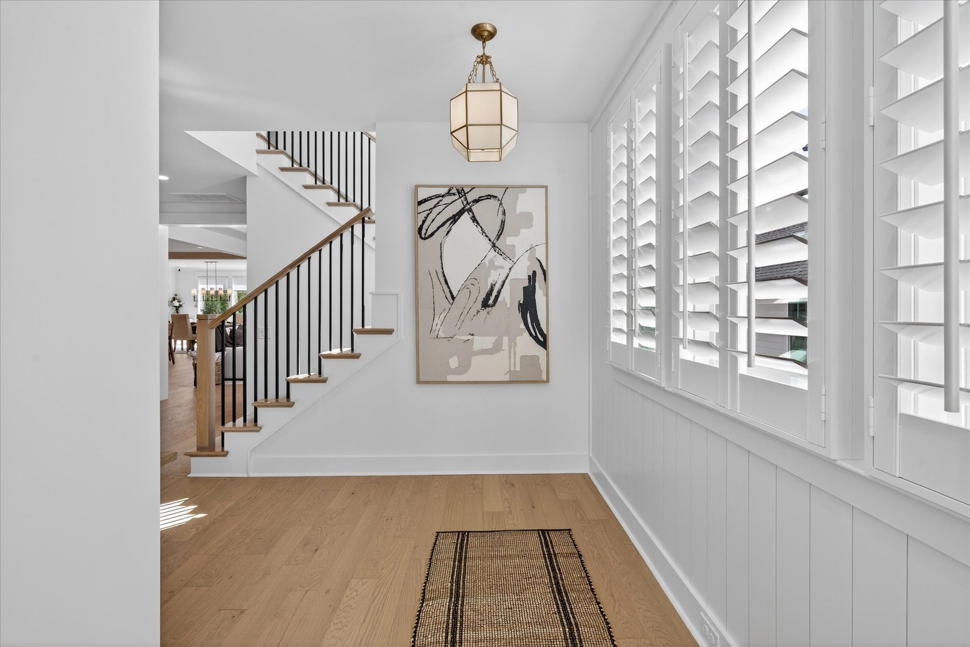 Bright entryway with white plantation shutters, wood staircase with black railings, and light hardwood floors