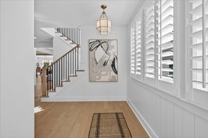 Bright entryway with white plantation shutters, wood staircase with black railings, and light hardwood floors