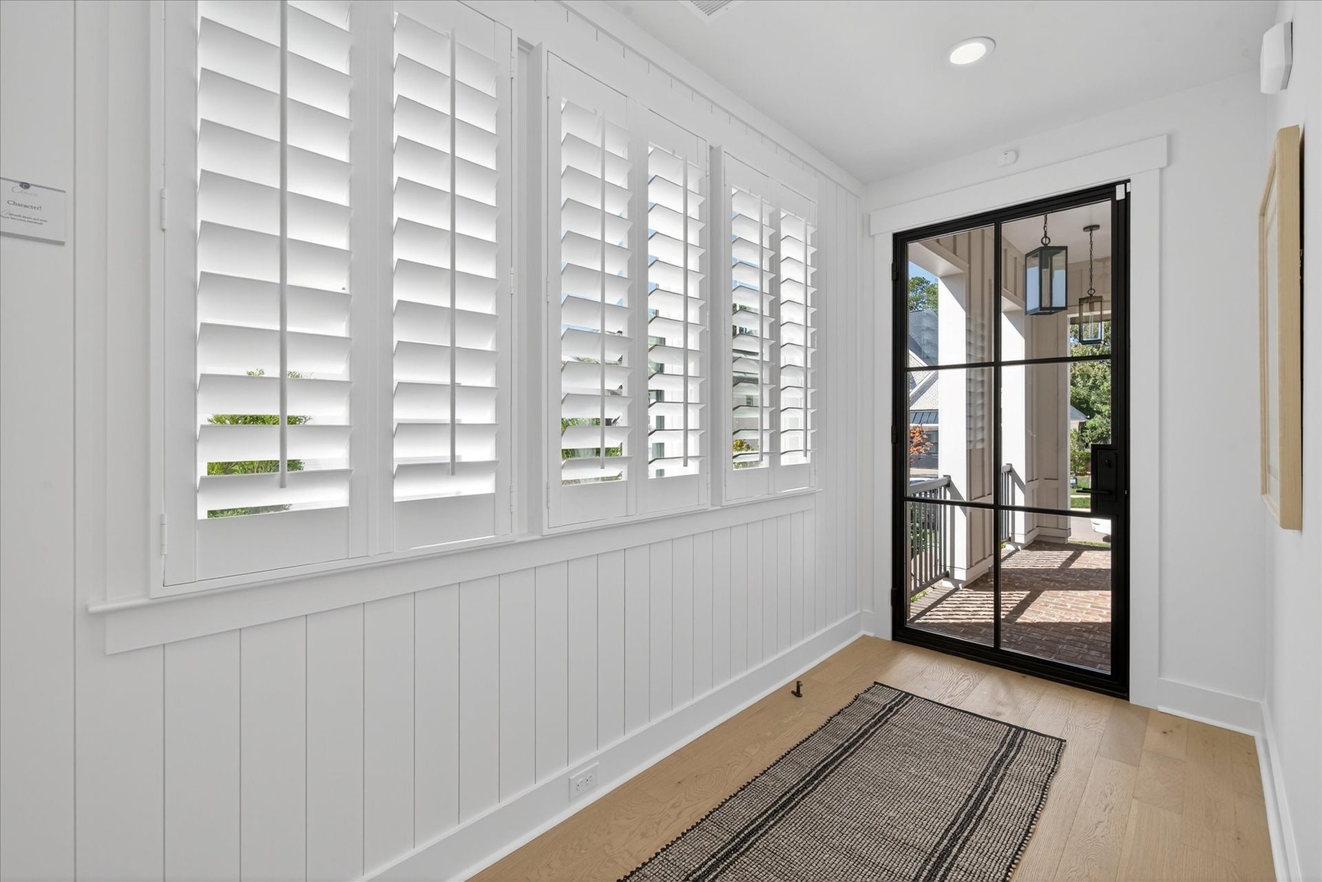 Bright entryway with white plantation shutters, black-framed glass door, and light hardwood floors