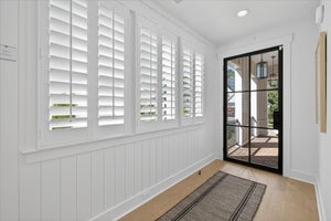 Bright entryway with white plantation shutters, black-framed glass door, and light hardwood floors