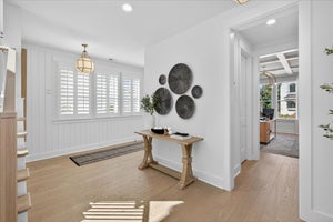 Bright entryway with white walls, light wood floors, console table, and decorative wall art