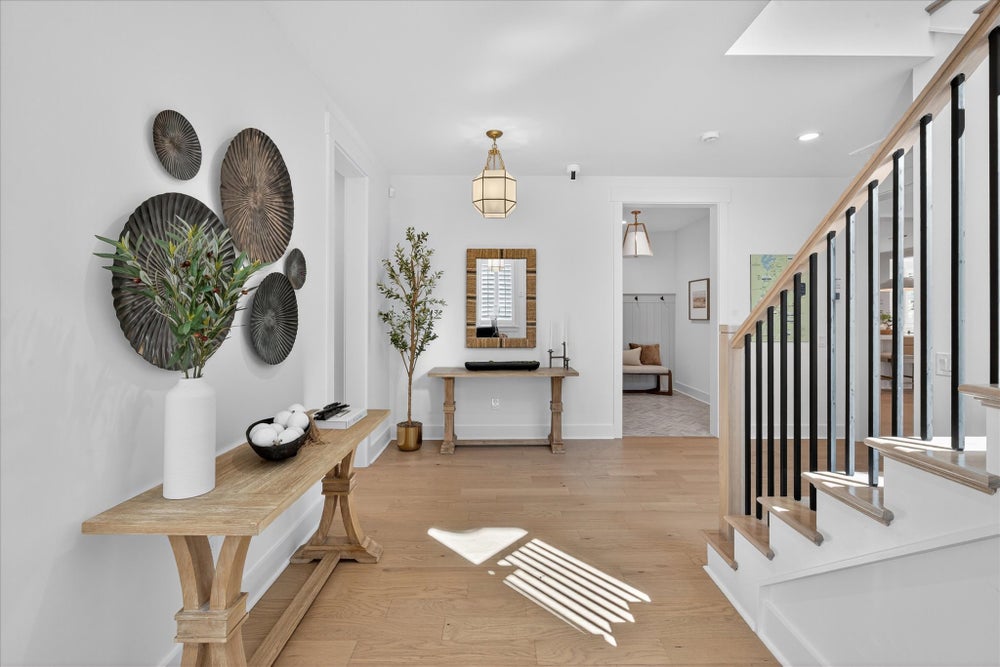 Modern entryway with light wood floors, decorative wall art, and staircase with black metal railings