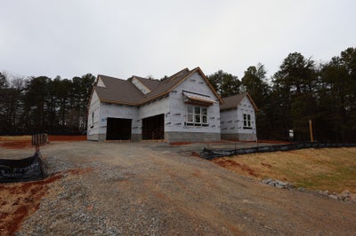 Single-story home under construction with house wrap and two-car garage on wooded lot