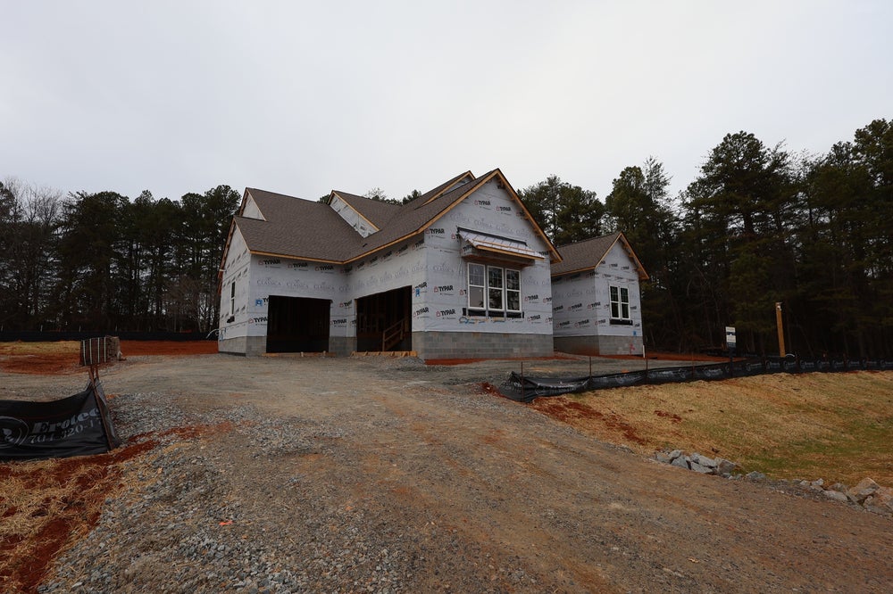 Single-story home under construction with house wrap and two-car garage on wooded lot