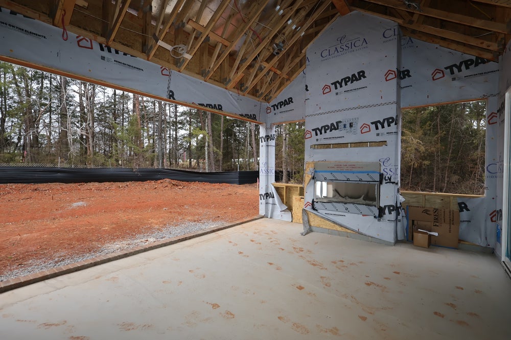 Home under construction with exposed framing, house wrap, and concrete garage floor