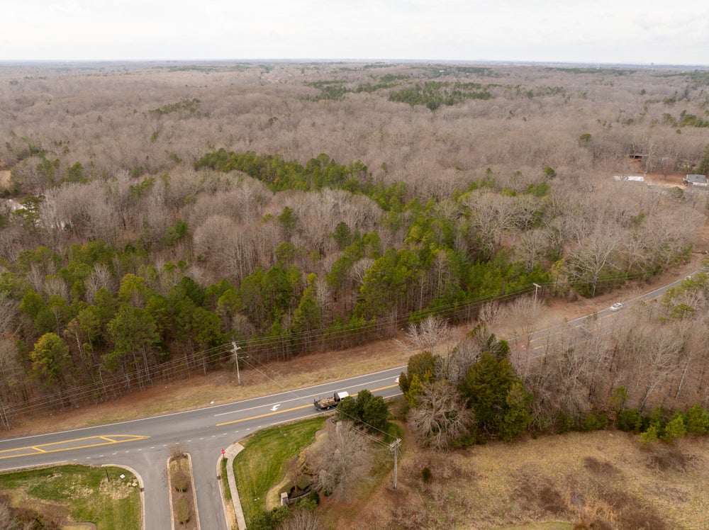 Aerial view of undeveloped wooded land with road access and rural surroundings